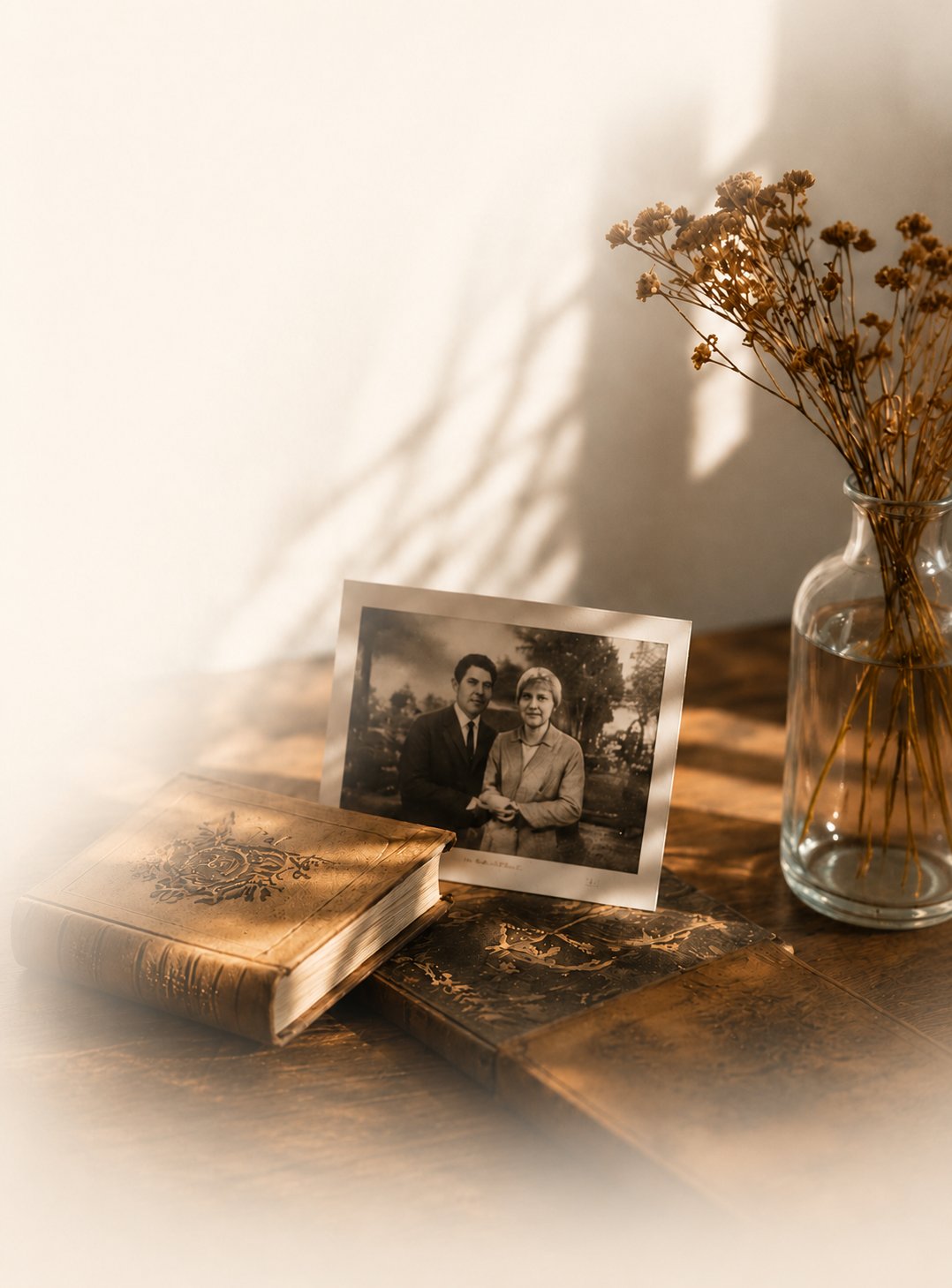 Una fotografía antigua de una pareja apoyada sobre libros encuadernados, junto a un jarrón con flores secas, iluminados por luz cálida de tarde.